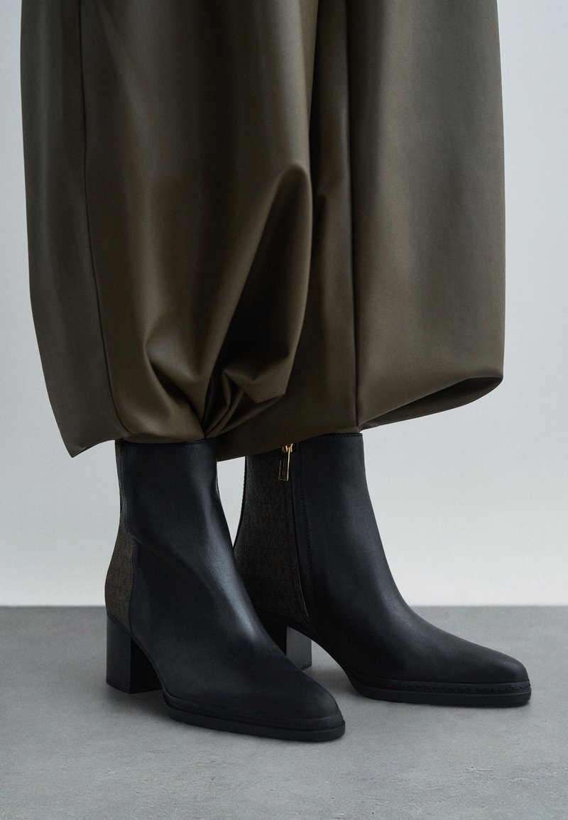 Bottines en cuir noir à talons carrés portées sous un pantalon large kaki.
