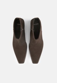 Bottines en daim marron avec un design épuré, bout carré et fermetures éclair latérales. Texture lisse avec des accents minimalistes et une silhouette structurée.
