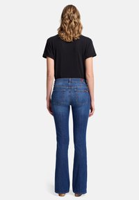 Jeans sbiaditi blu a campana con vita alta e due tasche posteriori, indossati con una maglietta nera larga. Texture in denim liscia.