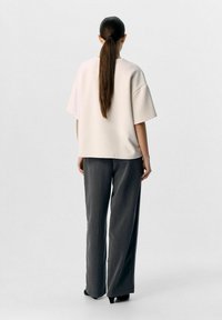 Ljusrosa, oversized kortärmad topp i kombination med mörkgrå vida byxor och svarta klackar. Slät textur och avslappnad passform.
