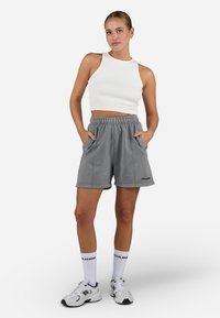 Gray cotton shorts with elastic waistband and side pockets, paired with a white ribbed crop tank top. White athletic shoes and socks.