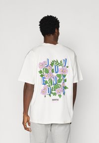 T-shirt branca de algodão com gráficos florais coloridos e texto em destaque a dizer "JUVENTUS" nas costas. Corte solto, mangas curtas, decote redondo.