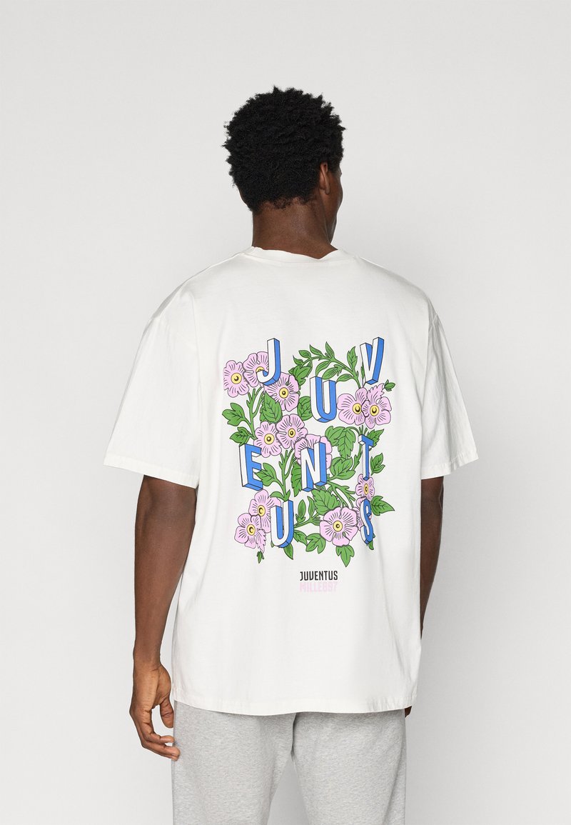 T-shirt branca de algodão com gráficos florais coloridos e texto em destaque a dizer "JUVENTUS" nas costas. Corte solto, mangas curtas, decote redondo.
