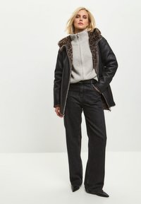 Sort læderjakke med leopardprintfor, grå ribstrikket sweater, højtaljede sorte jeans og spidse sorte sko.