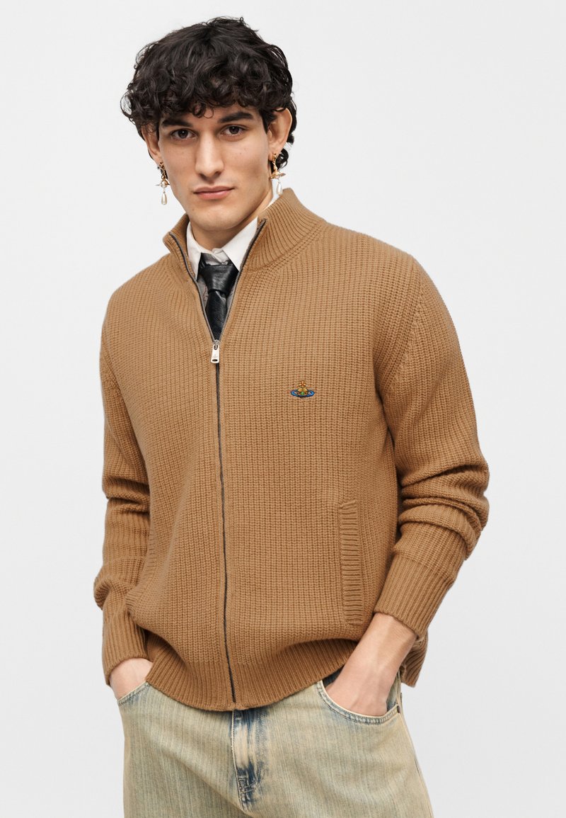 Brown knitted zip-up sweater with ribbed texture, high collar, two side pockets, and embroidered logo detail on the chest.