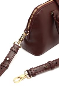 Sac en cuir bordeaux avec zip doré et accessoires en métal, doté d'une sangle amovible et d'une texture lisse. Les accents incluent un fermoir à crochet et des détails de couture.