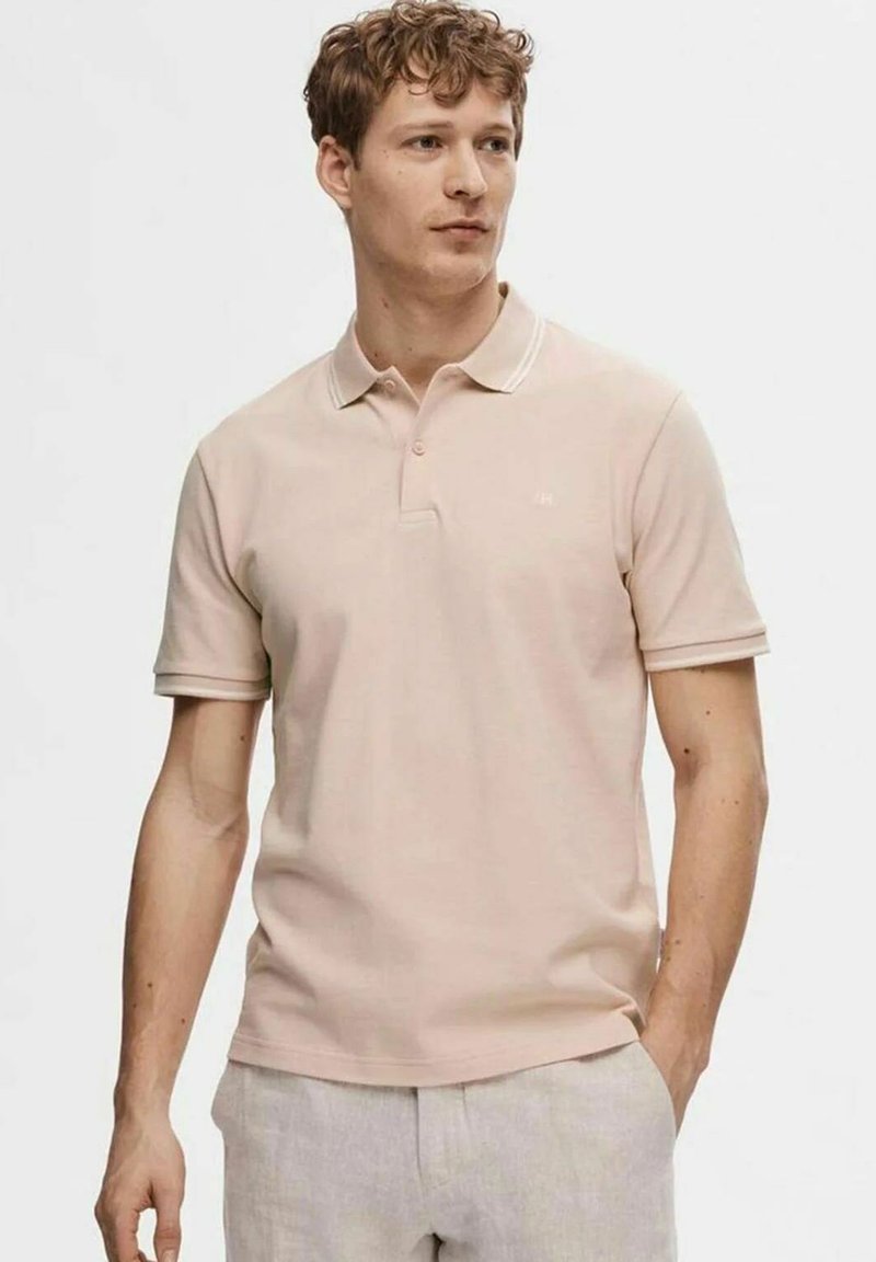 Polo shirt rosa chiaro con maniche corte, un colletto a due bottoni e cuciture bianche sottili lungo il colletto. La trama del tessuto è morbida e visibile.