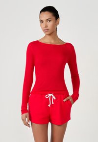Czerwony prążkowany top z długim rękawem i szerokim dekoltem, zestawiony z czerwonymi szortami z białym sznurkiem i bocznymi kieszeniami. Gładka faktura.