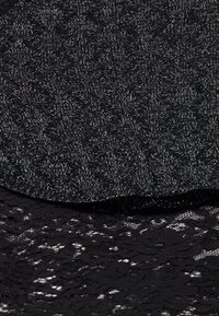 Zwarte stof met een gestructureerd breipatroon bovenop een doorschijnende kantlaag, met een delicate bloemdesign en een subtiele glans van metallic draden.