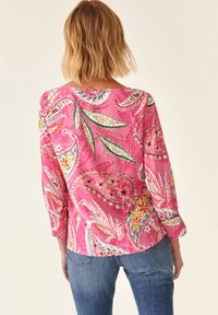 Blouse florale rose présentant un motif cachemire, des manches longues avec des poignets smockés et une coupe décontractée. Un tissu léger qui améliore le confort.