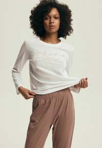 Biała koszulka z długim rękawem z nadrukowanym tekstem, połączona z jasnobrązowymi spodniami z elastycznym pasem. Gładki materiał i luźny krój.