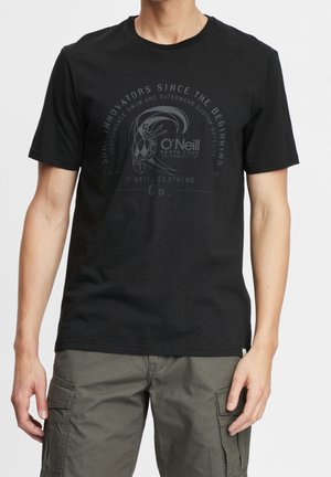Mężczyzna ubrany w czarną koszulkę O'Neill z okrągłym logo i graficznym napisem, w połączeniu z oliwkowozielonymi szortami typu cargo.