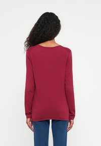 Bordeaux trui met lange mouwen, ronde hals en ribbelstructuur. Draagt met blauwe jeans, met een rechte silhouet en een relaxte pasvorm.