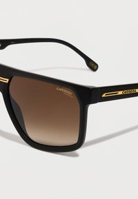 Occhiali da sole Carrera neri rettangolari con lenti marroni sfumate e dettagli in oro sugli steli e nell'angolo della lente.