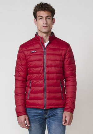 Chaqueta acolchada roja con patrón de acolchado horizontal, cuello alto y detalles en cremallera negra. Cuenta con dos bolsillos laterales con cremallera.