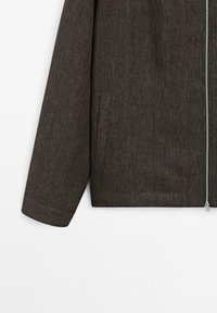 Brun zip-up jacka i texturerat material. Har en ståkrage, ribbade muddar och sidofickor. Minimalistisk design med rena linjer.