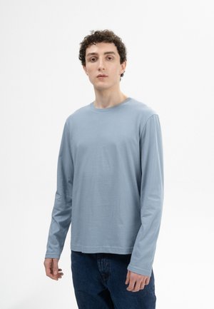 Helles blaues langärmliges T-Shirt aus weichem Material mit rundem Ausschnitt und geradem Saum, kombiniert mit dunkelblauen Jeans.