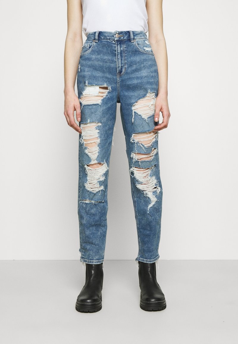 Sprängda blå denimjeans med hög midja, med flera slitna lappar och fransade kanter, tillsammans med svarta ankelstövlar.