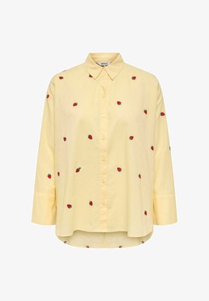 Chemise jaune boutonnée avec des fraises rouges brodées. Elle comporte un col, des manches longues, un ourlet arrondi et un tissu texturé.