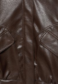 Nahaufnahme einer dunkelbraunen Lederjacke, die die strukturierte Oberfläche, die zentrale Naht und zwei Klappentaschen auf beiden Seiten zeigt.