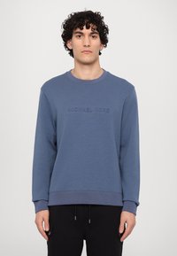 Sudadera azul hecha de una mezcla de algodón que presenta un cuello y puños acanalados, un logo grabado en la parte delantera y un corte relajado.