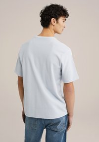 Ljusblå kortärmad t-shirt med en texturerad yta, rund hals och avslappnad passform. Bärs med blå jeans, vilket visar en avslappnad look från baksidan.