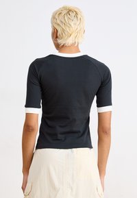 Svart tettsittende T-skjorte med korte ermer, hvite mansjettakenter og rund hals. Glatt stoff, minimalistisk design og ingen synlige logoer.