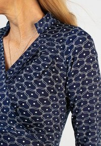 Tummansininen mekko, jossa valkoisia aaltoa muistuttavia viivoja ja pisteitä; siinä on mandariinikaulus ja pehmeä kangas, jonka kaula-aukon kohdalla on laskokset.