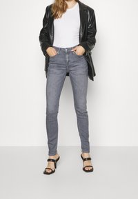 Jeans skinny de tiro alto grises combinados con una camiseta blanca ajustada y una blazer de cuero negra, llevada con sandalias de tacón negras.