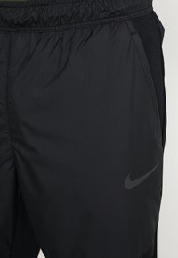 Mustat urheiluhousut, joissa on joustava vyötärönauha, valmistettu kevyestä kankaasta. Omistaa sileän pinnan ja mustan Nike-logon alaosassa.