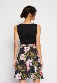 Black sleeveless top transitions to a floral skirt with pink and green patterns, featuring a flared design and smooth texture.