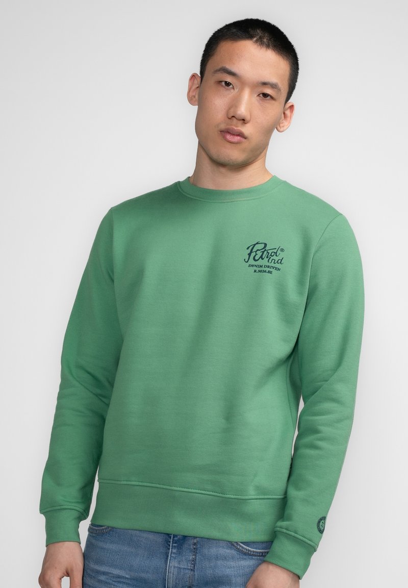 Sweatshirt vert avec encolure ras du cou, poignets et ourlet côtelés. Présente un logo imprimé sur le côté supérieur gauche de la poitrine. Texture de tissu douce.