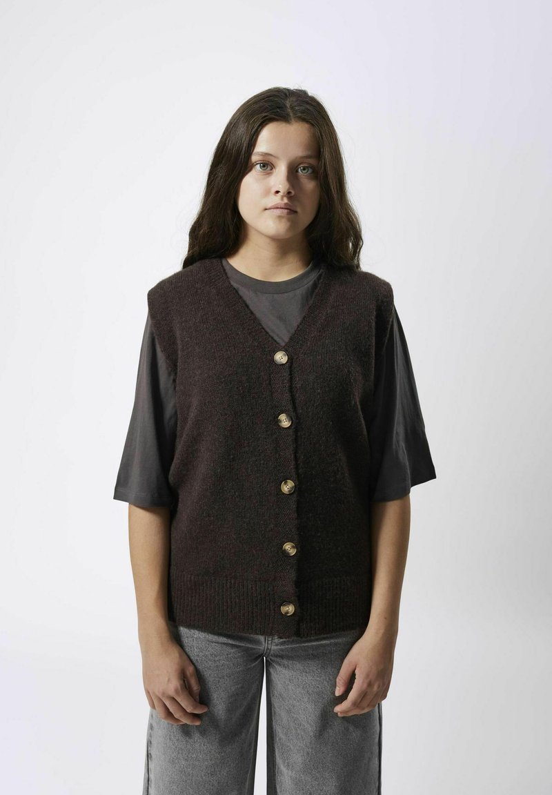 Dunkelbrauner gestrickter ärmelloser Pullover mit V-Ausschnitt, der sechs goldene Knöpfe auf der Vorderseite und einen gerippten Saum aufweist. Trägt man über einem dunkelgrauen Hemd.
