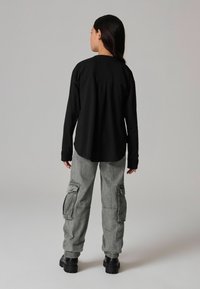 Zwarte langetermijn comfortabel shirt met een plooi aan de achterkant, gecombineerd met grijze cargo-broek met zakken en elastische boorden, gedragen met zwarte chunky laarzen.