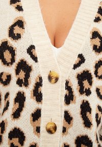Cardigan crema con motivo leopardato, caratterizzato da macchie nere e sabbiose. La parte frontale ha tre bottoni; il materiale sembra morbido con un lavorazione a maglia testurizzata.