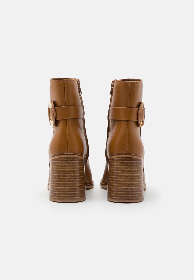 Bottes en cuir marron à la cheville avec un design arrondi, des zips sur les côtés et un large talon bloc avec une texture striée et une boucle décorative.