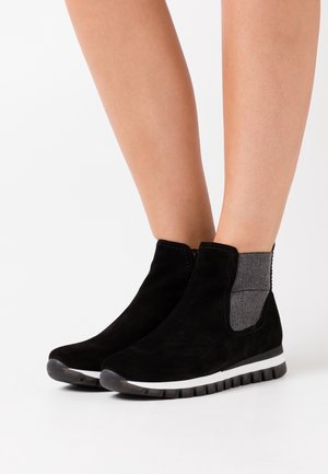 Stivali alla caviglia in suede nero con pannelli laterali elasticizzati grigi, punta rotonda e suola in gomma a strisce bianche. Progettati per comfort e flessibilità.