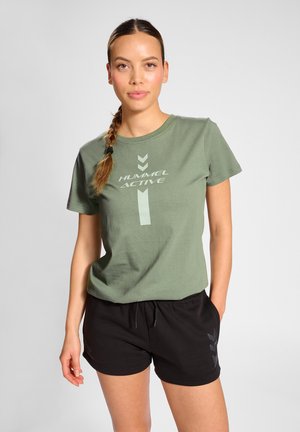 Grünes Baumwoll-T-Shirt mit kurzen Ärmeln, das ein hellgrünes Logo "HUMMEL ACTIVE" zeigt, sowie schwarze Shorts mit seitlichem Akzent und Kordelzug.