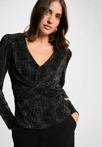 Top nero a maniche lunghe con scollatura a V profonda, caratterizzato da dettagli metallici e un design strutturato a pieghe. Stile avvolgente con vita cintrata.