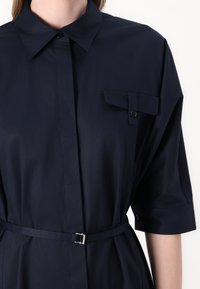Navy blue shirt dress made of smooth fabric, featuring a buttoned chest pocket, short sleeves, and a cinched waist with a metal buckle.