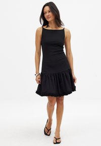 Vestido negro con un corsé ajustado y un dobladillo acampanado con volantes. Hecho de una tela suave. Presenta tirantes finos y un escote recto.