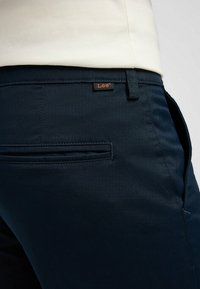 Pantalons bleu marine en tissu lisse dotés d'une fermeture à bouton et zip, de poches latérales et d'une poche arrière avec un détail logo Lee.