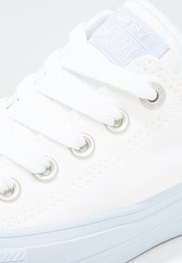 Baskets en toile blanche avec une surface texturée, des accents bleus sur la languette et des œillets argentés pour les lacets. Design classique à tige basse.