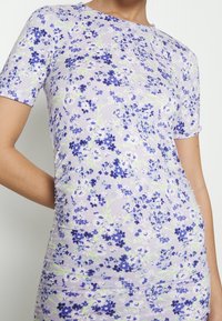 Fioletowa sukienka w kwiaty z krótkimi rękawami, z wzorem niebieskich i białych kwiatów na lawendowym tle, wykonana z elastycznego materiału.