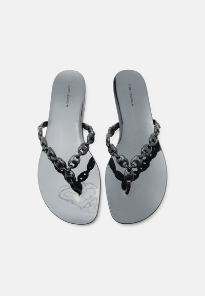 Γυαλιστερά μαύρα επίπεδα σανδάλια με λουράκια τύπου αλυσίδα και το «Tory Burch» τυπωμένο στη σόλα, τοποθετημένα πλάι-πλάι σε λευκό φόντο.