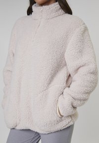 Fuzzy, ljusrosa tröja med hög krage och kvartdragkedja. Har sidofickor och ett mjukt, texturerat fleecematerial.