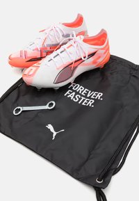 White and pink soccer cleats with black accents, accompanied by a black drawstring bag featuring the text "FOREVER. FASTER." and a silver wrench.
