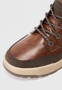 Bruna lädersneakers med mörkbruna accenter och strukturerad mellansula. Har rundad tå, snörning fram och kontrasterande sömmar.