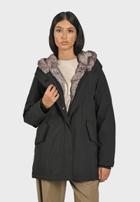 Černá parka s kapucí podšitou umělou kožešinou, se zapínáním na zip a knoflíky a dvěma předními kapsami. Hladký vnější povrch, design po kolena.