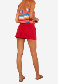 Top sin mangas a rayas de colores con tirantes finos, combinado con shorts rojos. Tejido suave y ligero; ajuste casual y relajado; sandalias planas visibles.